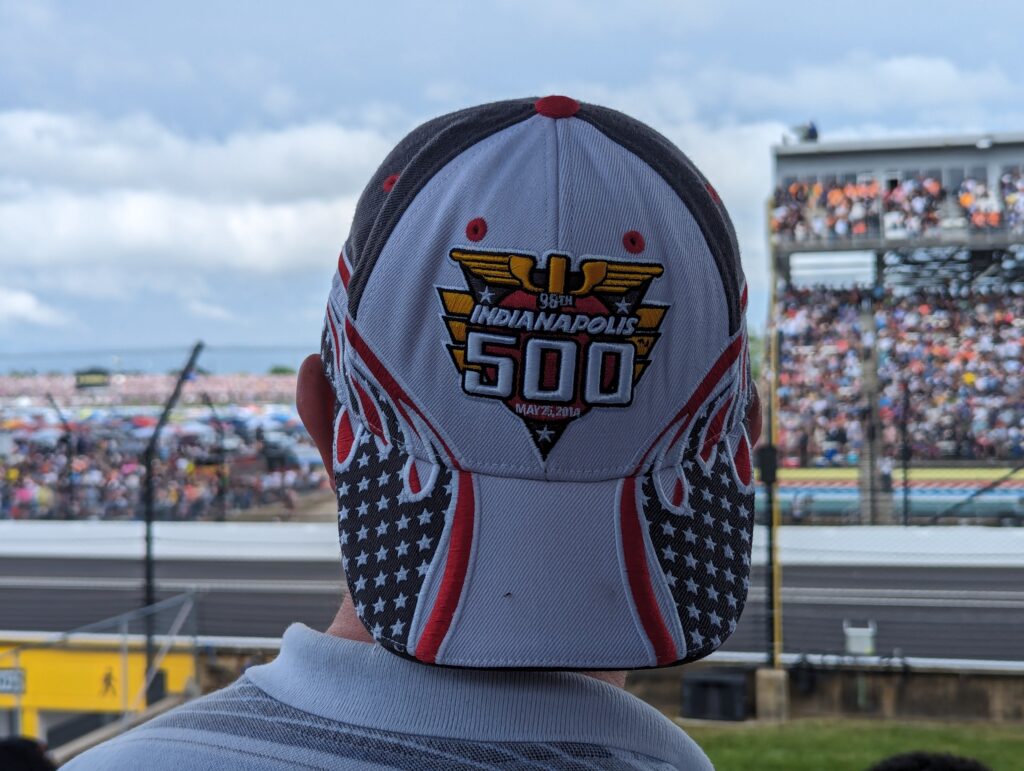 Simon B wearing a cap with the Indianapolis 500 logo, facing the race track.