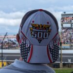 Simon B wearing a cap with the Indianapolis 500 logo, facing the race track.