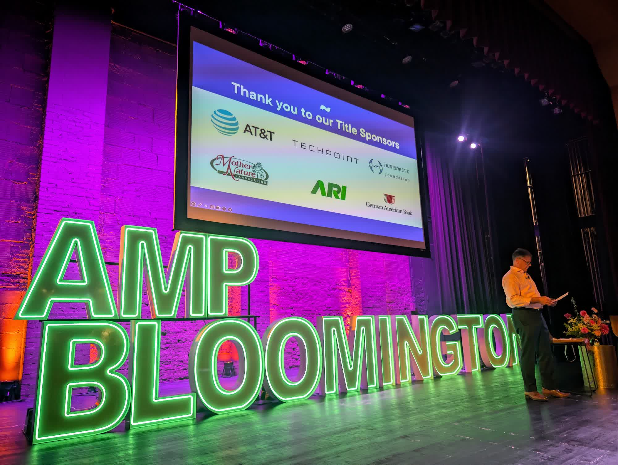 Slide thanking the AMP Bloomington title sponsors including AT&T and TechPoint, with a speaker standing at the edge of the stage
