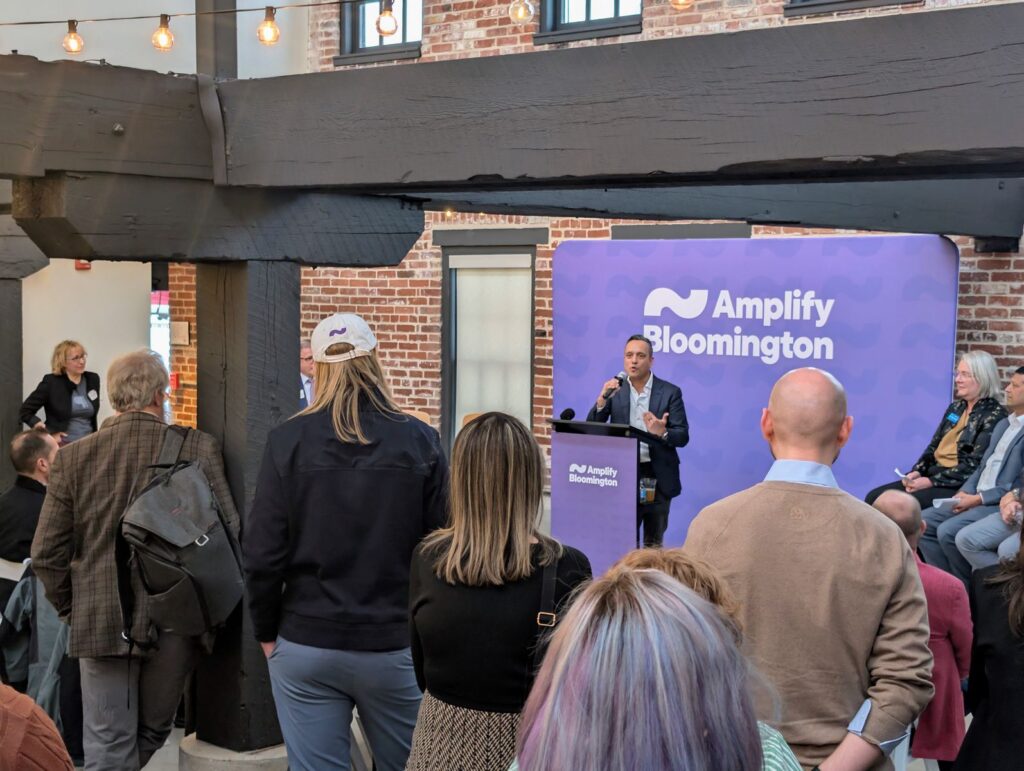 Speaker at a podium at the Amplify Bloomington launch event with an audience in the foreground