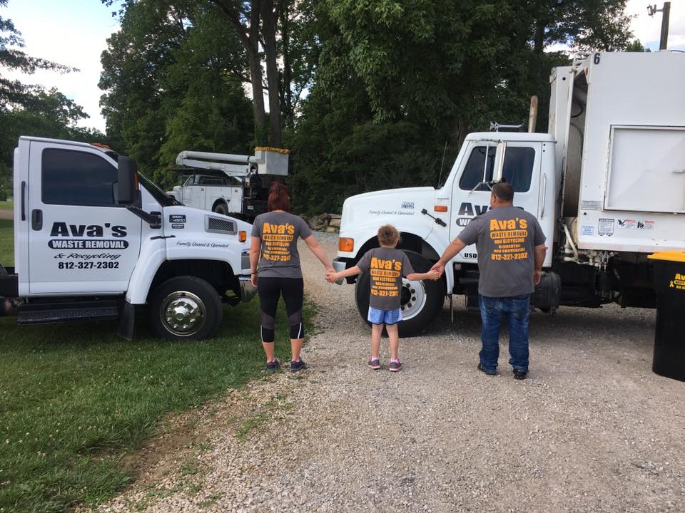 Family members of Ava’s Waste Removal holding hands between two company trash trucks in Bloomington, Indiana