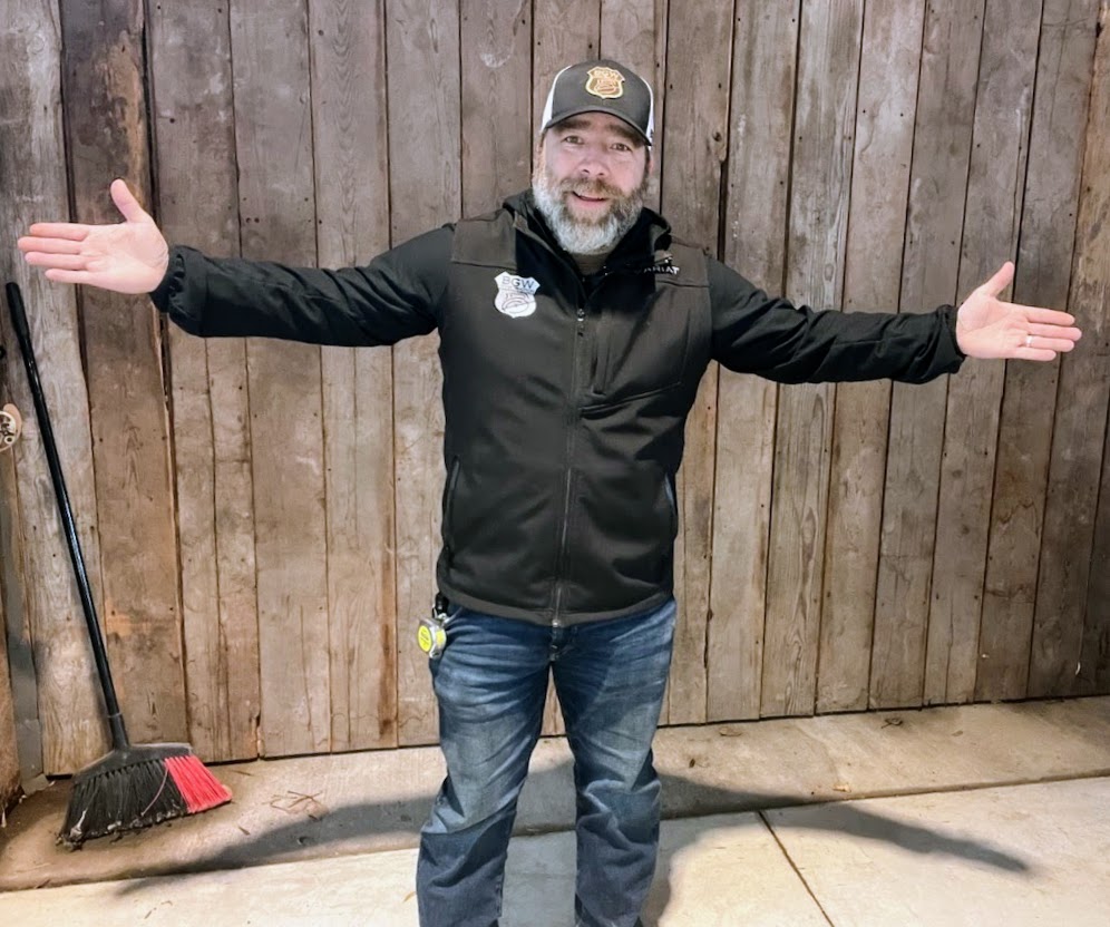 Bobby Williams standing with his arms open in front of wood workshop doors.