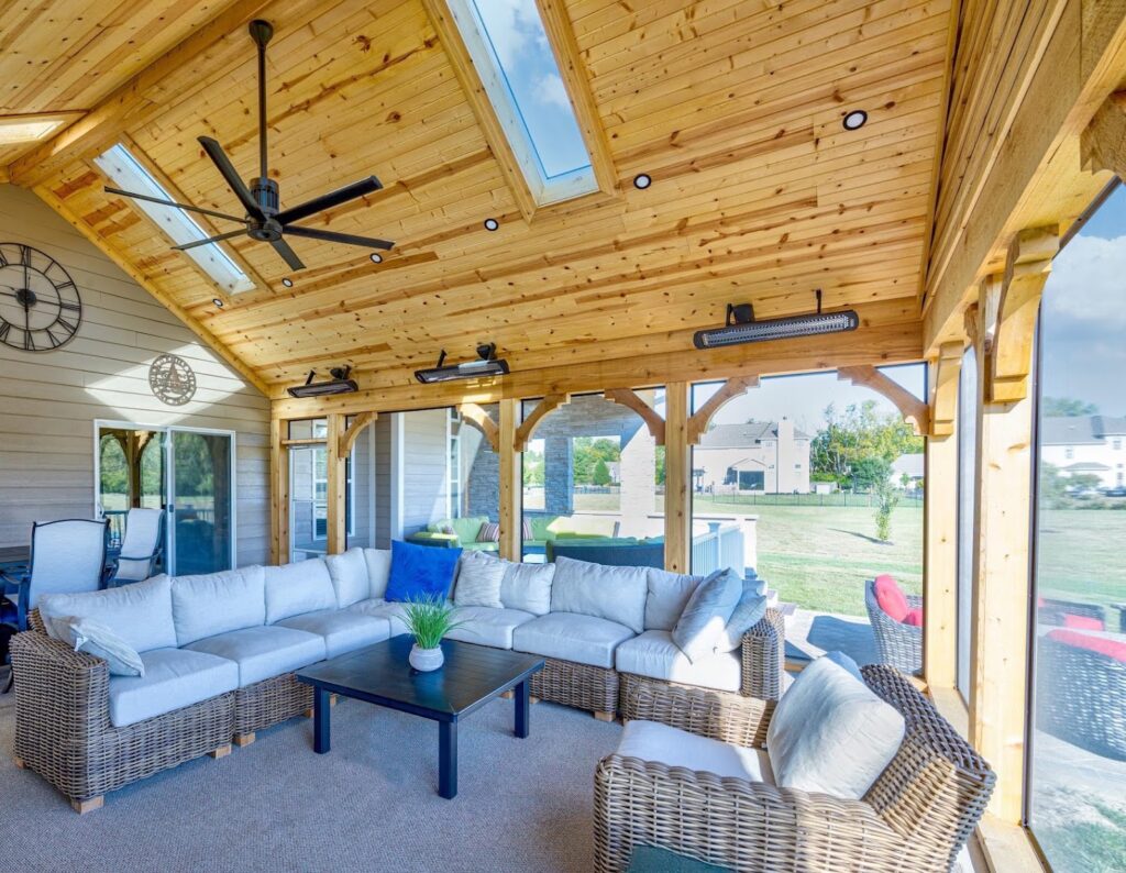 Screened porch with a vaulted wood ceiling, skylights, ceiling fan, mounted heaters, and sectional seating.