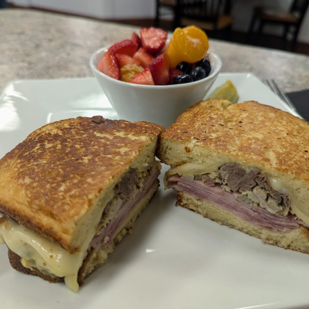 Close-up of a Cuban sandwich with layers of ham, pork, and melted cheese served with a side of fresh fruit at Brightside Cafe.