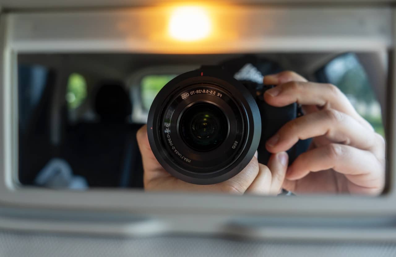 Close-up view of a camera lens held by a photographer reflected in a car's rearview mirror, symbolizing professional photography services in Bloomington, Indiana.