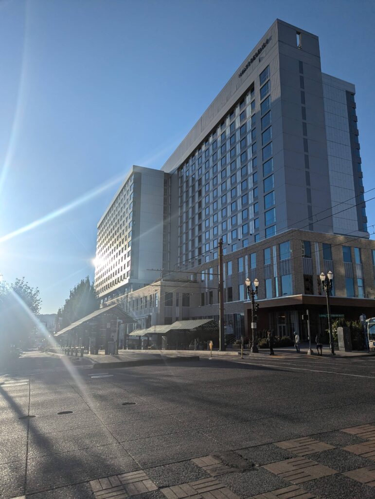 The exterior of the Hyatt Regency in Portland, Oregon, with sunlight reflecting off its tall glass windows. This hotel served as the main accommodation for WordCamp US 2024 attendees.