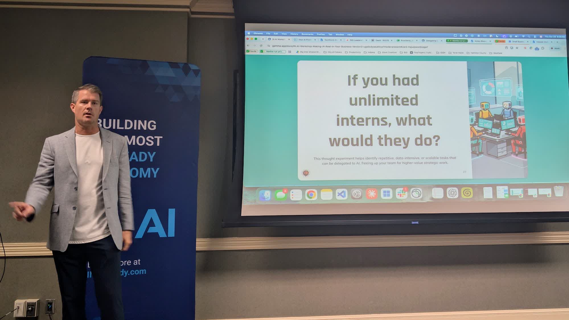 Colin Stauffer, in a gray blazer, stands beside a projected slide that asks If you had unlimited interns, what would they do