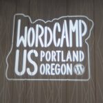 A projected logo for WordCamp US 2024 displayed on a wall at the Oregon Convention Center in Portland, Oregon, featuring the WordPress logo.